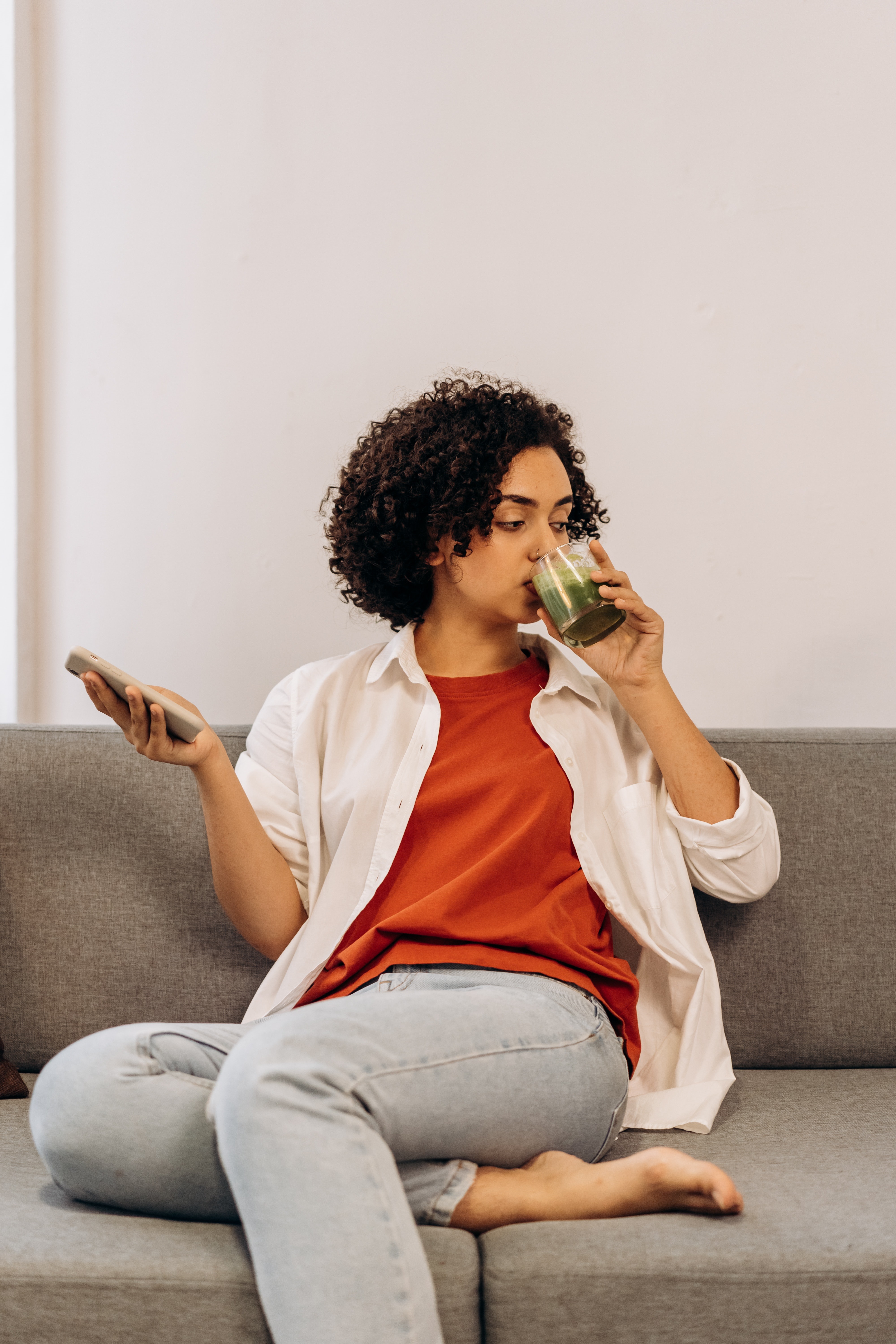 Woman Sitting on Couch Drinking Green Juice